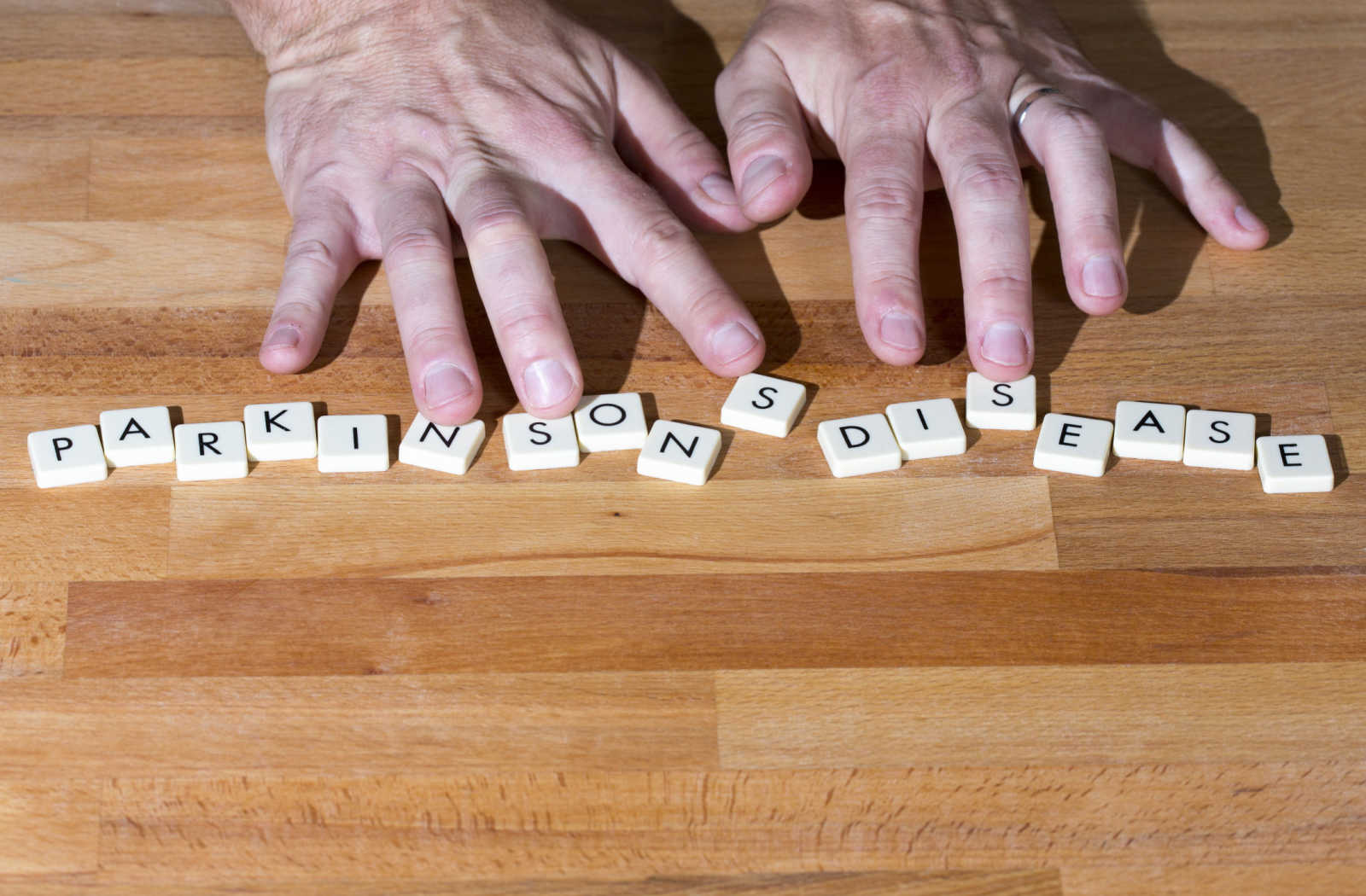 A seniors hands placed above block letters on a table spelling out parkinsons disease.