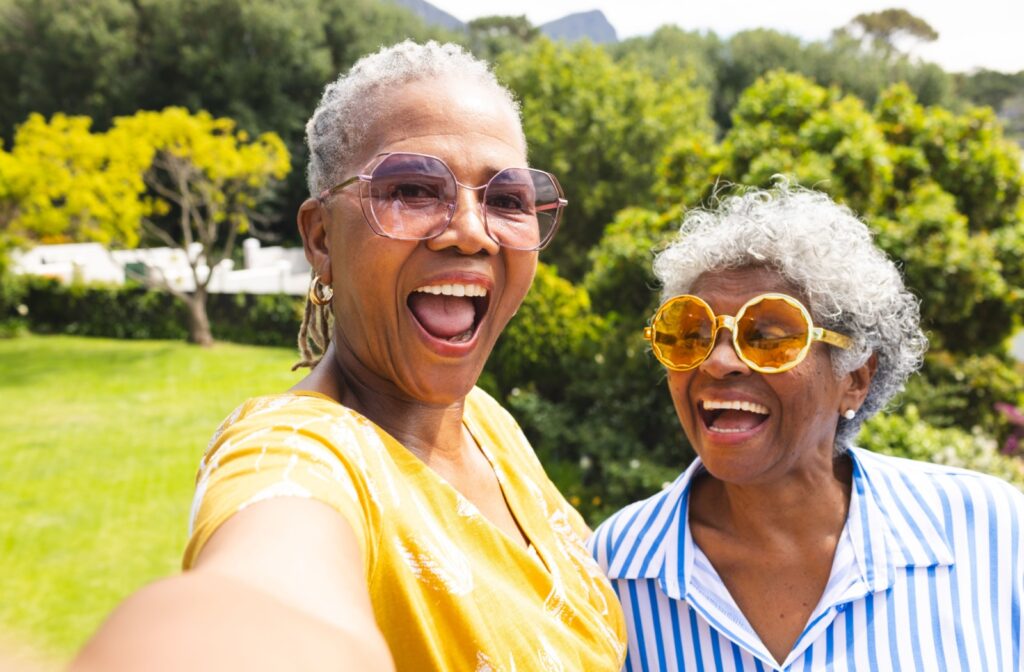 Two older adults laugh while taking a picture together, celebrating their friendship while hanging outdoors together.