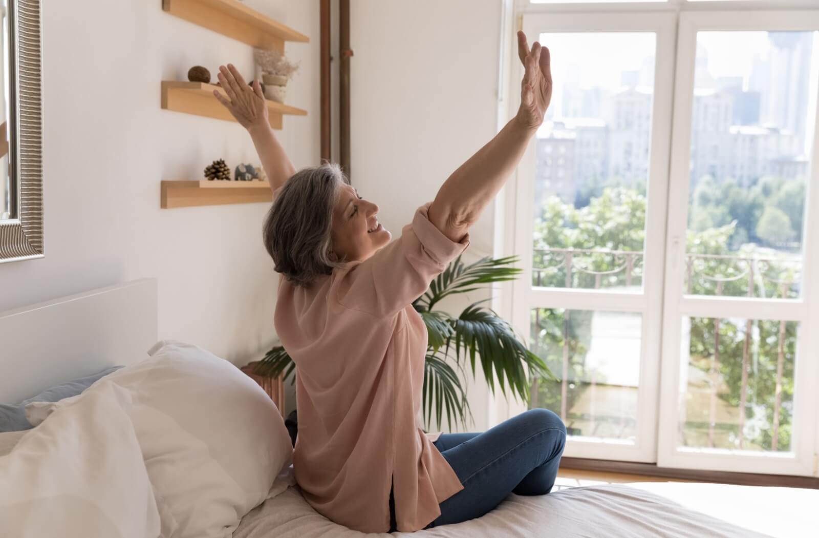 An older adult stretching in front of their window in the morning after a good night's rest.