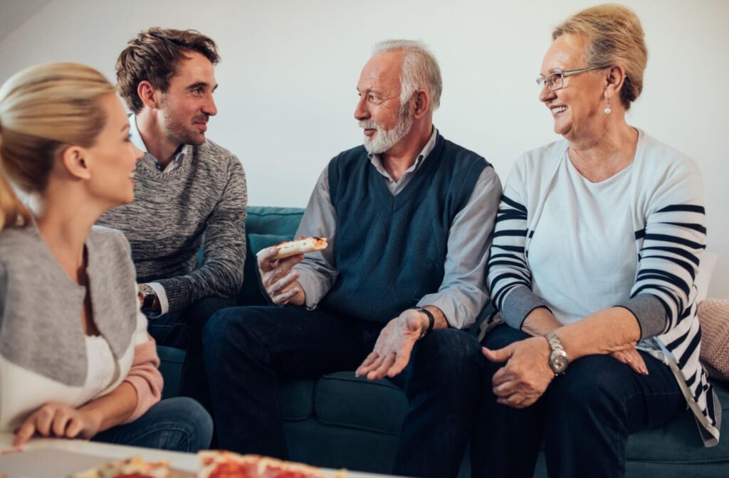 Two older parents laughing with their adult children over pizza during a visit to assisted living.