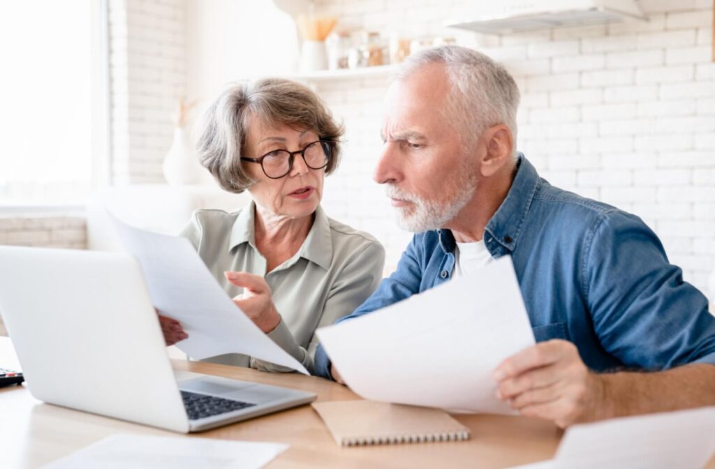 An older couple in a serious discussion while sorting through paperwork and researching potential senior living communities at their kitchen table