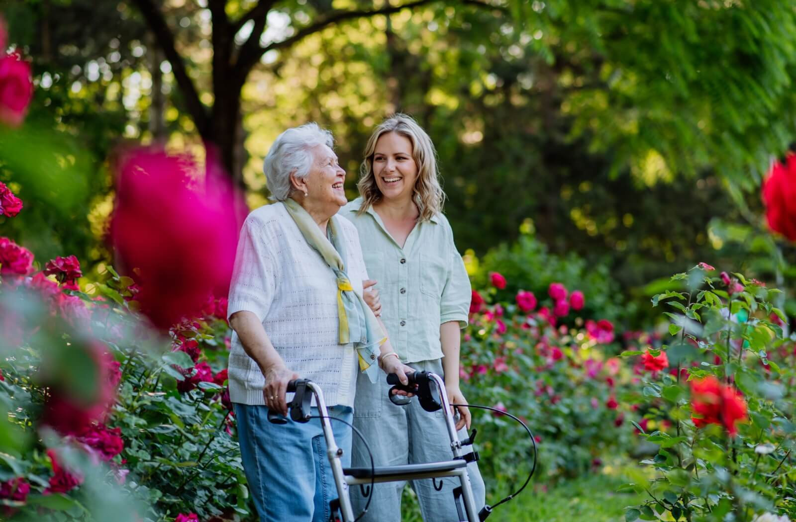 A senior uses a walker to enjoy the outdoor garden with an adult child during a visit to their senior living community