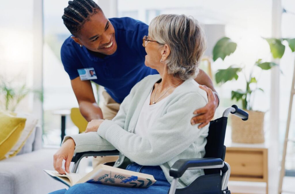 A senior living caregiver smiles at a senior in a wheelchair while bending down to check in with them on their daily needs